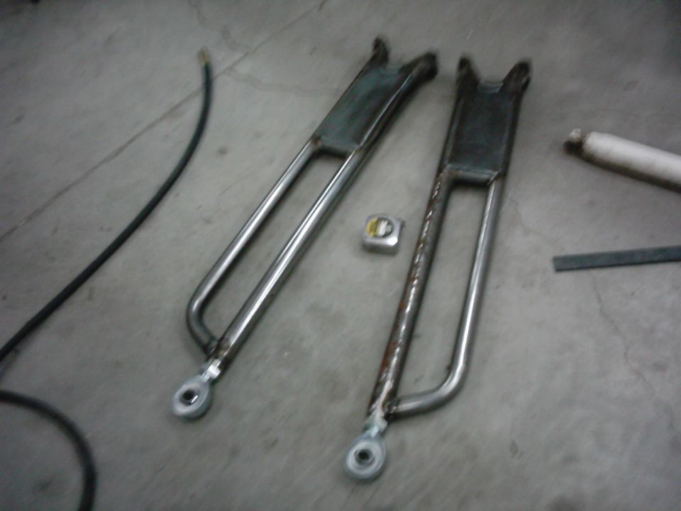 two metal radius arms on a concrete floor with a tape measure