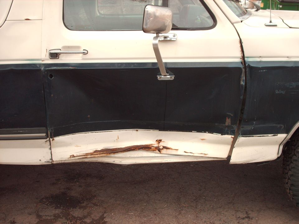 1988 Ford Bronco side door with significant rust and damage along the lower body panel