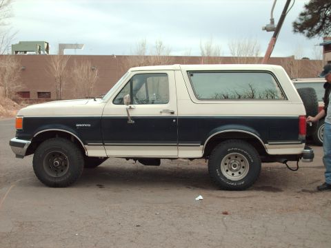 1988 Ford Bronco - A two-tone blue and white Ford Bronco is parked outdoors, showing its side profile.