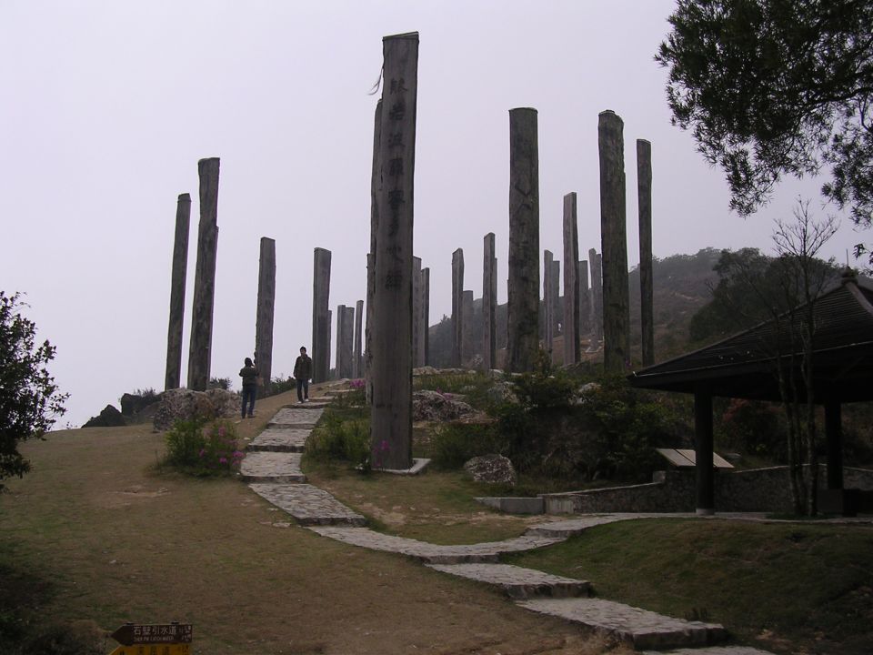 Stone pillars and a pavilion on a misty hillside with a paved path