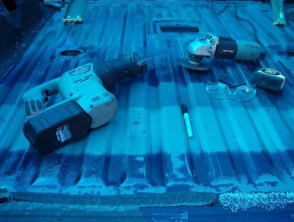 Cordless reciprocating saw and angle grinder on a blue-tinted truck bed