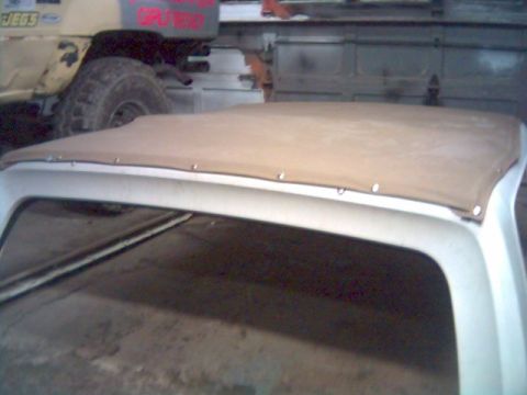 1986 Ford Bronco - A tan soft top is secured to the frame of a white vehicle, with another vehicle visible in the background.