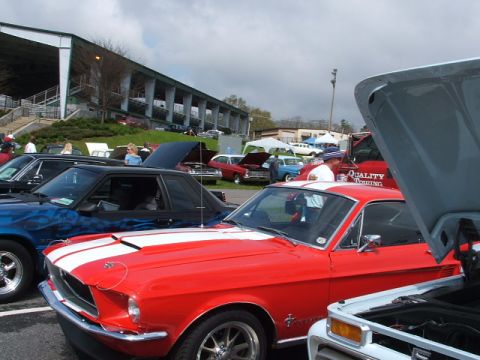 1966 Ford Ranchero - A red 1967 Ford Mustang with white racing stripes is displayed at a car show.