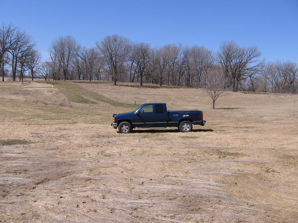 1995 GMC Sierra 1500 pickup truck parked in a field with bare trees and blue sky
