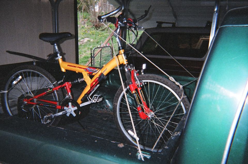 Yellow and red mountain bike secured in the bed of a green pickup truck