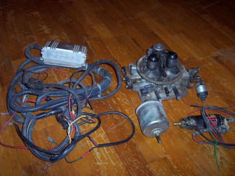 1974 Ford Bronco - Automotive parts including a carburetor, ECM, and wiring are displayed on a wood surface.