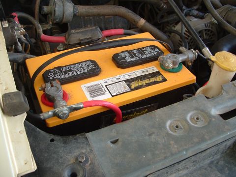 1990 Ford Bronco - Orange Duralast Gold battery sitting in the engine bay with heavy red and black 4-gauge cables clamped to lead top-post terminals, a green…