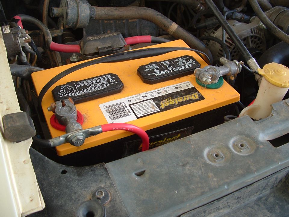 Orange Duralast Gold battery in engine bay with red and black cables and Bussmann fuse block
