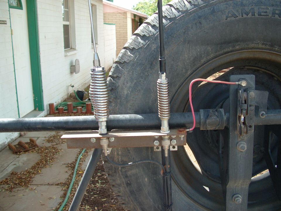 Two CB antennas mounted on a spare tire carrier with a large tire behind