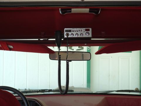 1990 Ford Bronco - A CB radio is mounted above the rearview mirror inside a vehicle with red interior trim.