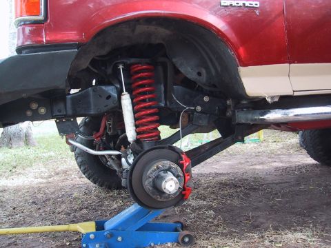 1990 Ford Bronco - Close-up view of the lifted suspension and front wheel assembly of a red Ford Bronco.