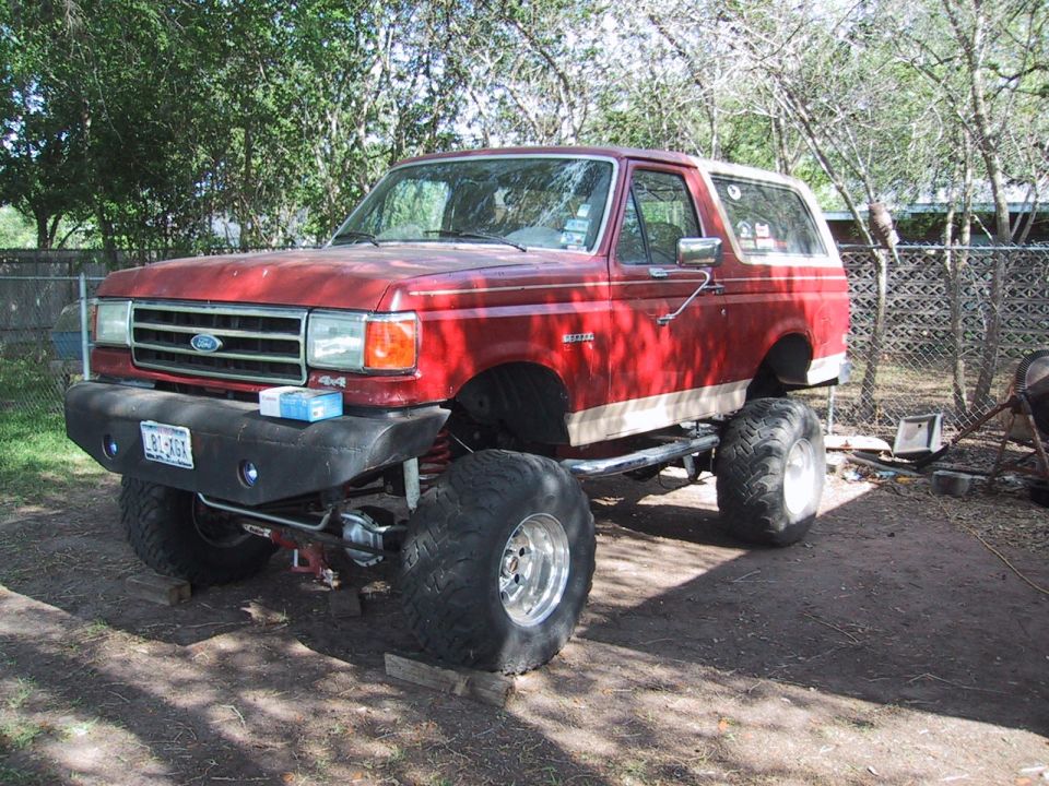 Red lifted 1990 Ford Bronco with large tires and custom bumper