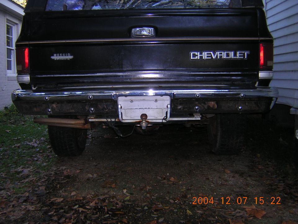 Black square-body Chevrolet pickup tailgate with chrome step bumper and ball hitch