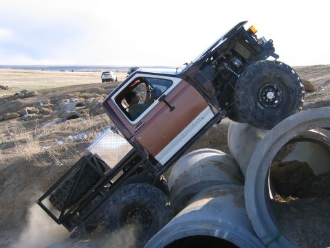 1981 Ford Bronco - A modified 1981 Ford Bronco navigates a challenging off-road course, climbing over large concrete pipes with another vehicle visible in the…