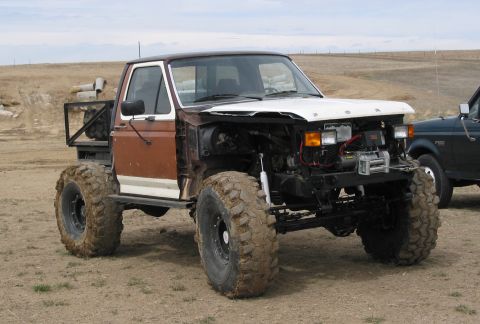 1981 Ford Bronco - A heavily modified truck with oversized tires and exposed engine sits in a dirt lot next to another vehicle.