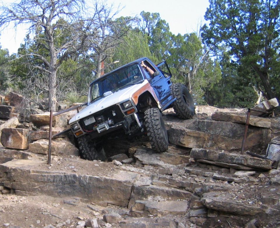 Chopped white and brown Ford 4x4 with winch climbing a rock ledge on a trail