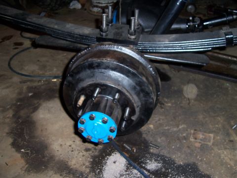 1983 Ford Bronco - Close-up view of a rear axle assembly, leaf springs and a brake drum with a bright blue hub cap.