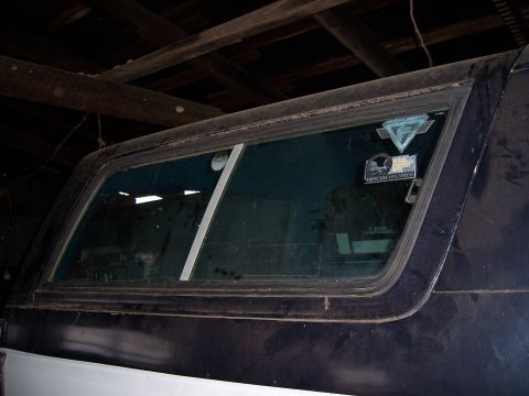 1983 Ford Bronco - Vehicle's rear side window with stickers visible on the glass.