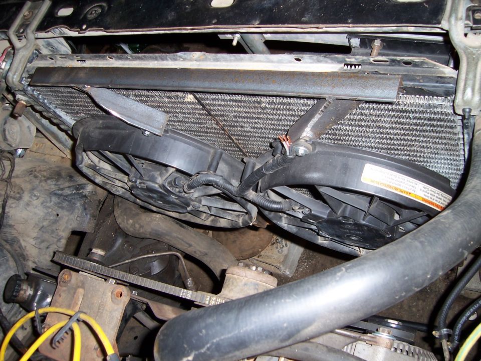 Close-up of two electric fans mounted in front of a radiator, with hoses and belts visible