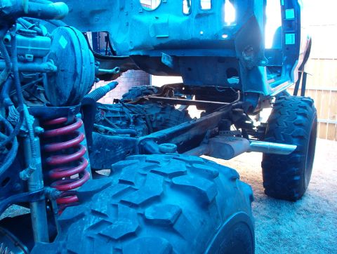 1994 Ford Bronco - The chassis and suspension components of a vehicle are visible, with large off-road tires and red coil springs.