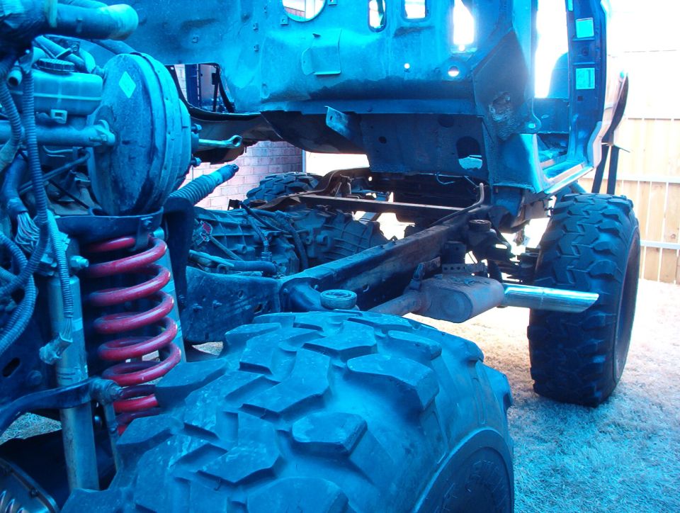 Lifted 4x4 frame and suspension with red coil springs and off-road tires, blue-tinted photo