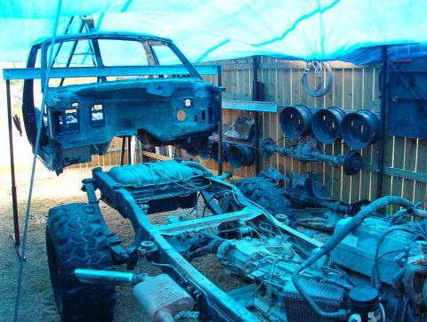 1994 Ford Bronco - A vehicle is disassembled with its body lifted and chassis exposed, surrounded by spare parts.
