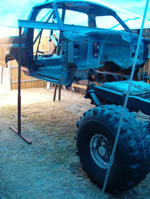 1994 Ford Bronco - A disassembled Ford Bronco body is elevated on a stand, revealing its chassis and a large off-road tire.