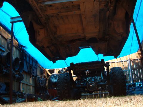 1994 Ford Bronco - The underside of a vehicle is visible, suspended for maintenance, with large tires and a blue tarp in the background.