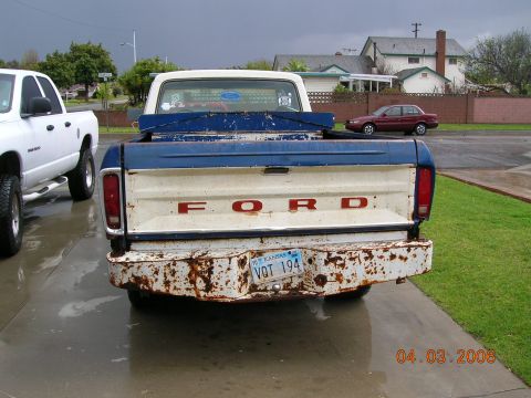 1985 Ford Bronco - A weathered Ford F-Series truck is parked next to a white pickup, with houses in the background.