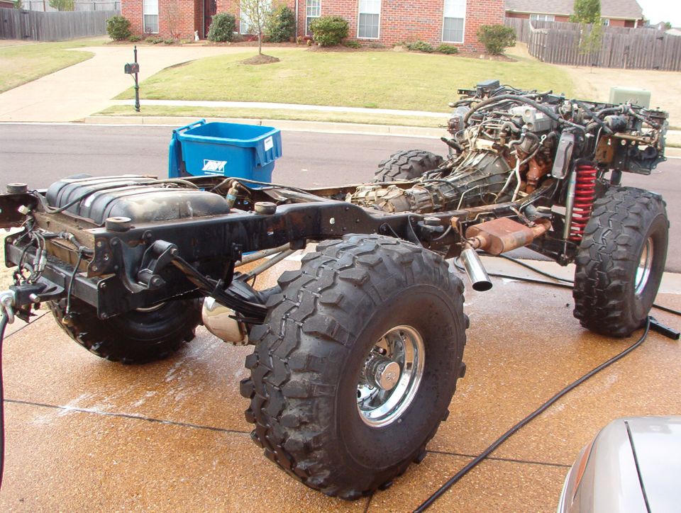 Bare truck frame with engine, big mud tires and chrome wheels on a driveway