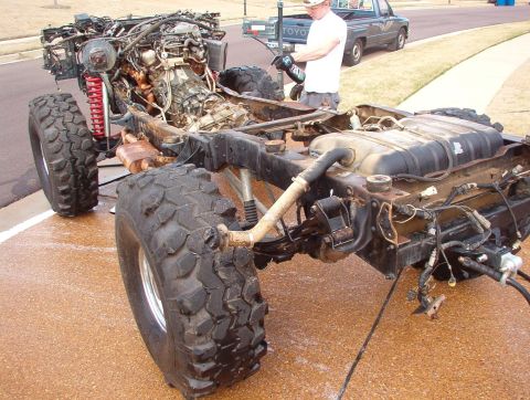 1994 Ford Bronco - The chassis of a heavily modified off-road vehicle is shown with its engine and fuel tank exposed, while a person works on it.