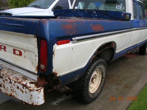 1985 Ford Bronco - Rusty Ford F-Series pickup truck with a white truck partially visible behind it.