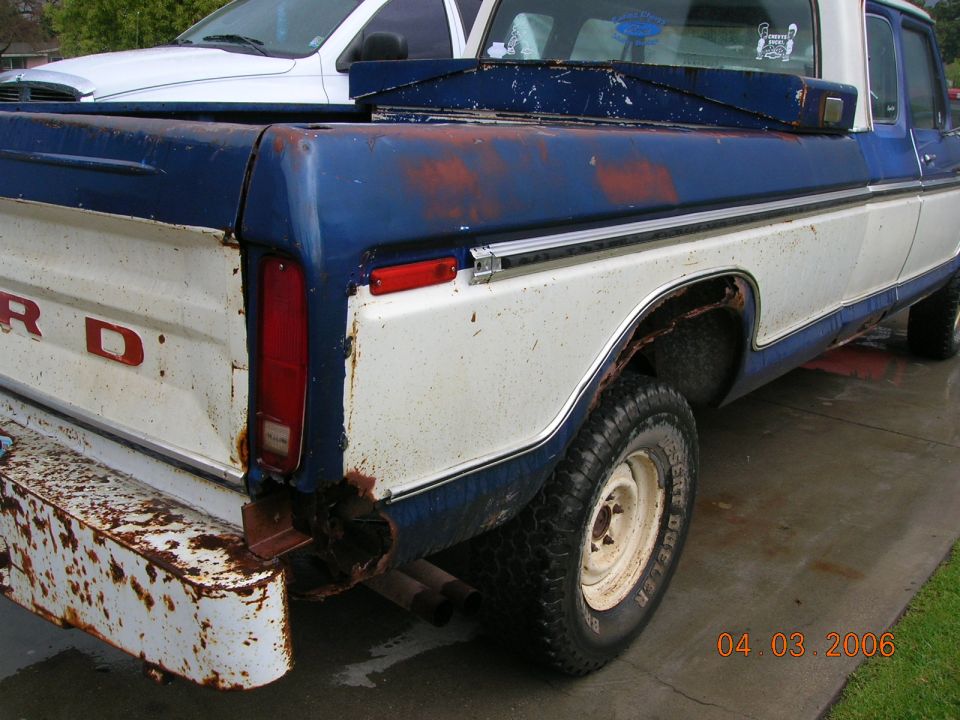 Rear quarter view of a rusty blue and white Ford F-Series pickup truck with a white truck behind it