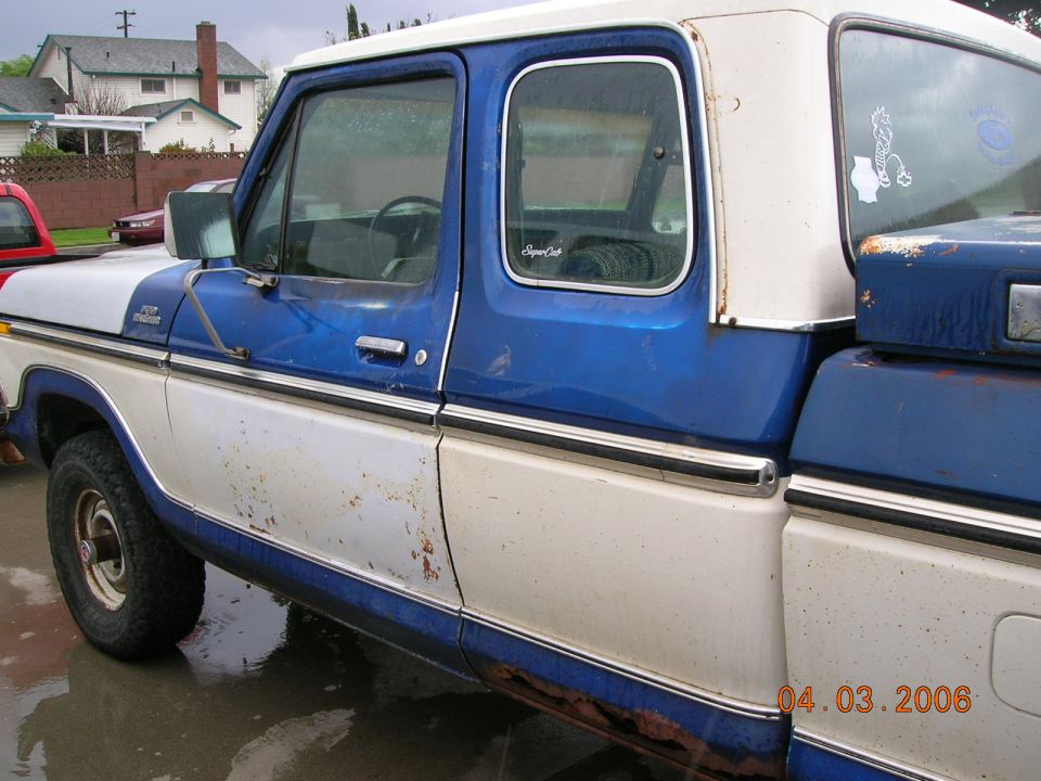 Blue and white Ford F-150 pickup truck, showing rust and wear, side view