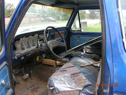 1985 Ford Bronco - The interior of a blue truck shows a damaged dashboard with missing gauges and a torn seat cover.