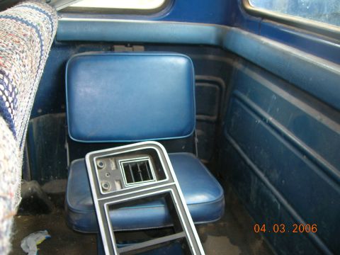 1985 Ford Bronco - The interior of a blue vehicle shows bench seats and a detached center console with air vents.