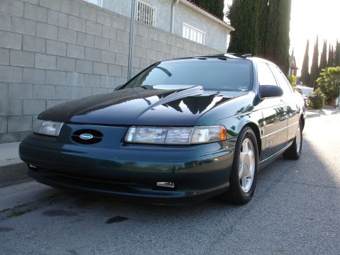 1993 Ford Taurus - A dark green sedan is parked on a residential street, angled towards the camera.
