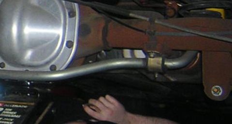 1998 Ford Crown Victoria - Underside of a vehicle showing a polished rear differential cover, exhaust piping, and a bare foot in the background.