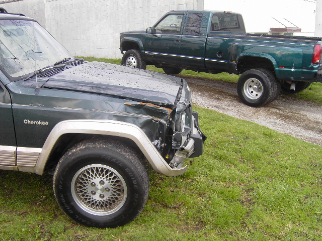 Damaged dark green Jeep Cherokee with 'Cherokee' badge, front quarter view