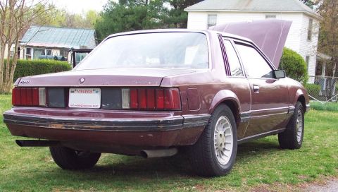 1985 Ford LTD Crown Victoria - This maroon Ford Mustang is parked on a grassy lawn with a house in the background and the hood is open.