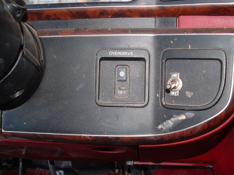 1990 Ford Bronco - Close-up of a woodgrain-trimmed center console showing an OVERDRIVE control with a D/OFF rocker switch, alongside a metal toggle switch (ma…