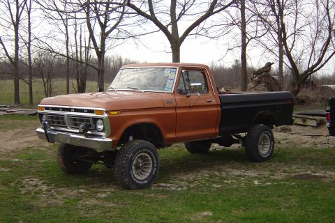 1977 Ford F-150 - This lifted 1977 Ford F-150 pickup truck is shown in a 3/4 front view, with its distinctive orange and black paint scheme.