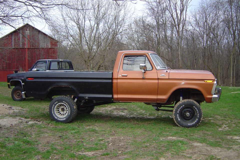 1977 Ford F-150 pickup truck with orange cab and black bed, parked next to a black pickup truck