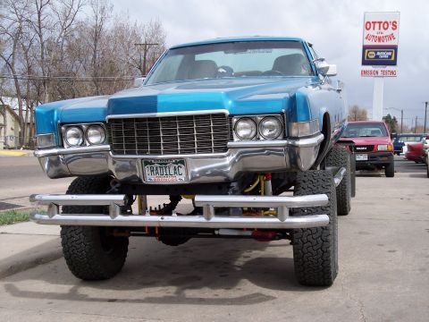 1972 Ford Ranchero - A heavily modified blue Cadillac sits high on its suspension, parked in front of an automotive service center.