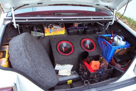 1985 Ford LTD Crown Victoria - The trunk of a 1985 Ford Crown Victoria LTD contains audio equipment, a spare tire, and storage crates filled with supplies.