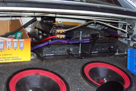 1985 Ford LTD Crown Victoria - The trunk of a car is filled with multiple audio amplifiers and two large subwoofers.