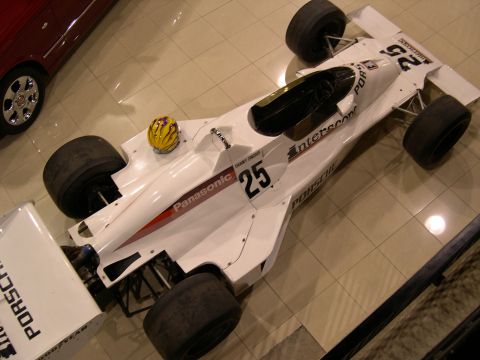 2002 Ford Focus - A white Formula 1 race car with "Panasonic" and "Porsche" branding is displayed indoors next to a red car.