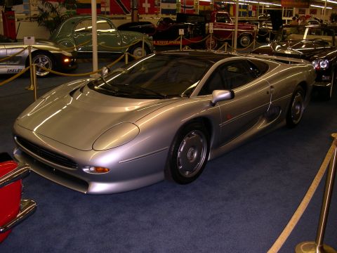 2002 Ford Focus - A silver Jaguar XJ220 sports car is displayed indoors, with other vehicles and flags in the background.