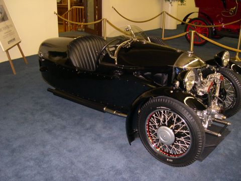 2002 Ford Focus - A vintage three-wheeled automobile is displayed indoors next to a red vehicle.