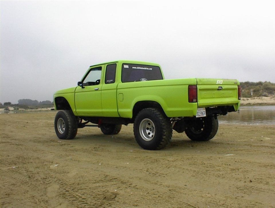 Lime green 1986 Ford Ranger pickup truck, rear 3/4 view, lifted on beach